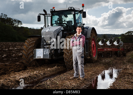 Ritratto di un giovane agricoltore con trattore e aratro in un campo arato. Foto Stock