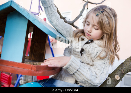 Ragazza giovane con birdseed su un albero nel giardino Foto Stock