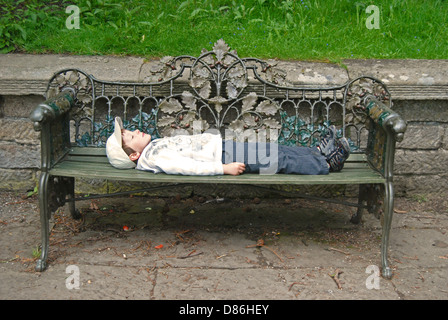 Un piccolo ragazzo disteso su un ornati in panchina da giardino Foto Stock