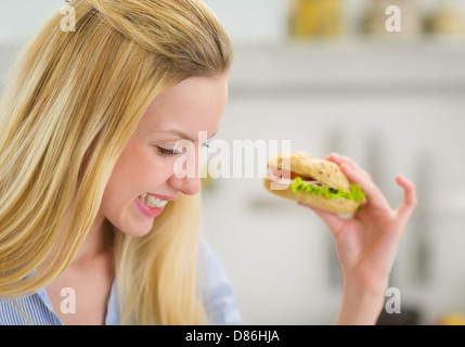 Felice giovane donna mangiare panino in cucina Foto Stock