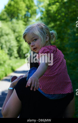 Una ragazza sorridente - figlia ottenendo un piggy back da sua madre nel parco Foto Stock