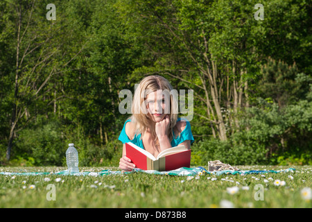 Ritratto di giovane e bella donna libro lettura sdraiati sull'erba a park Foto Stock