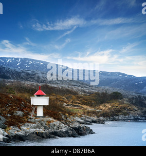 Faro norvegese. Torre bianca con parte superiore rossa sorge su rocce costiere sotto il cielo blu Foto Stock