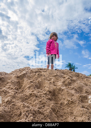 Regina della pila di sabbia. Una giovane ragazza ispanica gioca sulla sommità di un grande mucchio di sabbia in un cantiere edile a Luque, Paraguay. Foto Stock