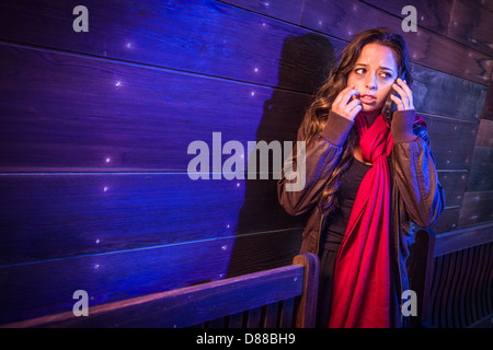 Frightened giovane donna in passerella scuro tramite telefono cellulare di notte. Foto Stock