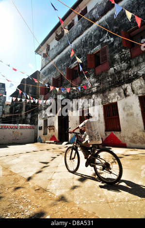 Un giovane ragazzo in sella alla sua moto nelle vecchie strade di Stonecity sotto il rosso, blu e bandiere bianche Foto Stock