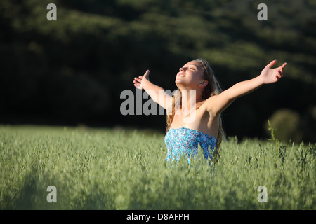 Bella ragazza adolescente felice di respirazione con bracci sollevati in un prato verde con uno sfondo scuro Foto Stock