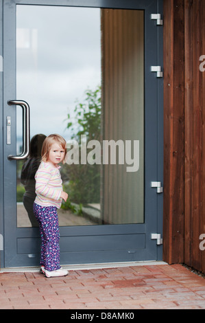 La foto all'aperto della bambina in attesa che qualcuno nella parte anteriore della porta Foto Stock