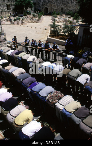 Poliziotti israeliani guardia come Palestinesi pregano gli uomini al di fuori al Akza moschea dopo aver bandito per accedere al Monte del Tempio composto durante la preghiera del Venerdì nella città vecchia di Gerusalemme Est Israele Foto Stock