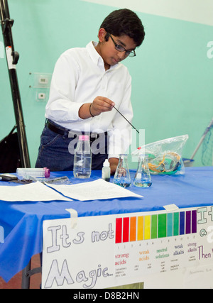 Maschio di studente di scuola superiore del medio oriente, decente utilizza bicchiere durante la fiera della scienza di dimostrazione Foto Stock