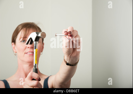 Donna che utilizza un martello per bang un chiodo in una parete Foto Stock