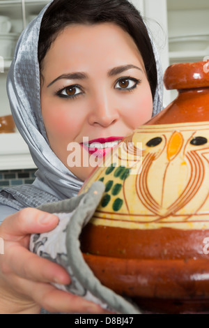 Marocchina tradizionale donna immigrati in Europa tajine di cottura durante il Ramadan nella sua cucina moderna Foto Stock