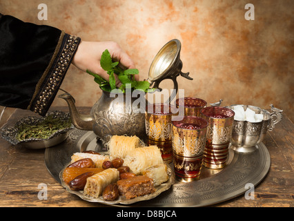 Femmina aggiungendo a mano le foglie di menta per un vassoio con date, biscotti e tè stile marocchino Foto Stock