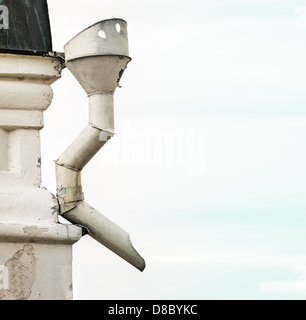 Bella casa con tubo di scolo curvo. Bianco fognatura inossidabile annesso all'edificio con tetto nero, sky in background. Weathered Foto Stock