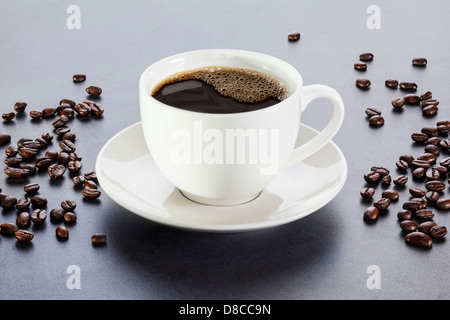 Tazza di caffè - caffè espresso o caffè nero su sfondo grigio, con i chicchi di caffè sparsi intorno. Anteriore per la regolazione del back focus. Foto Stock