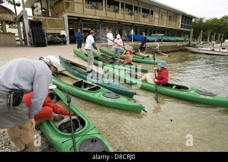 L'immagine mostra un gruppo di kayak che preparano le loro attrezzature prima di uscire in acqua. Il kayak è uno sport all'aperto che prevede la navigazione di una piccola barca, o kayak, attraverso corpi d'acqua. È popolare per attività ricreative, sportive ed esplorative. I kayak spesso praticano misure di sicurezza, tra cui indossare giubbotti salvagente e controllare le loro attrezzature prima di iniziare un viaggio. Foto Stock