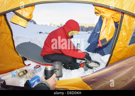 Uomo che indossa una calda giacca rossa cucinando fuori sulla neve di aprire la porta della tenda su un ghiacciaio in montagna. Chamonix Francia Europa Foto Stock