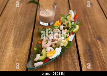 Cocktail di gamberetti con avocado, uova, succo di limone e un bicchiere di salsa su un tavolo di legno. Foto Stock