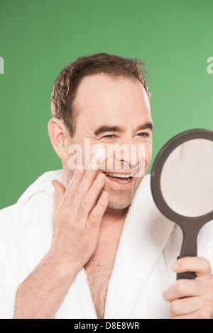 Felice l'uomo in accappatoio l'applicazione di crema per il viso Foto Stock