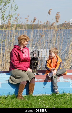 Una madre e il suo giovane figlio e il loro cane seduto su una barca accanto al lago, Schaalsee Zarrentin, Meclemburgo-Pomerania Occidentale, Germania Foto Stock