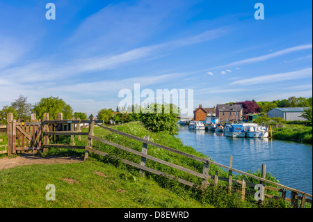 Scafo sul fiume con barche ormeggiate lungo la banca con la scherma e case su una luminosa giornata soleggiata con cielo blu, il Yorkshire, Regno Unito. Foto Stock