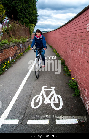 Donna caucasica matura in bicicletta su un percorso ciclabile stretto. Foto Stock