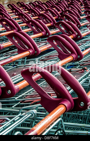 Primo piano delle maniglie arancioni e rosse delle file di carrelli per lo shopping dei supermercati ben parcheggiati fuori dal supermercato Sainsbury's del Regno Unito. Foto Stock