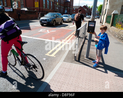 Giovane ragazzo in attesa ad un semaforo per cross road mentre la persona sulla bicicletta procede in attraversamento pedonale in Cardiff Wales UK KATHY DEWITT Foto Stock