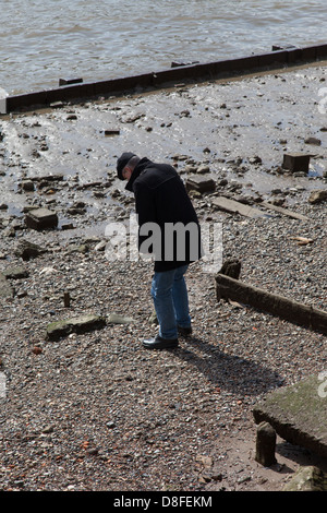 Uomo che indossa hat ricerca su foreshore a bassa marea, il fiume Tamigi e Londra Foto Stock