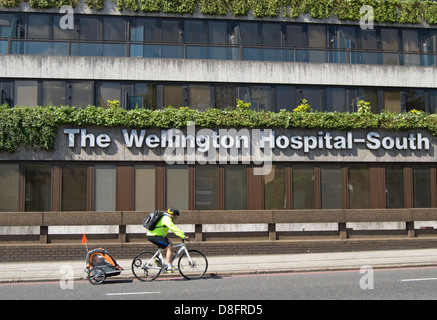 Ciclista maschio con un giovane ragazzo in corse rimorchio passato l'ospedale di Wellington, St Johns Wood, Londra, Inghilterra Foto Stock