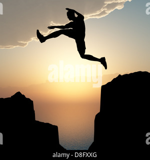 Silhouette dell'uomo di salto da una roccia Foto Stock