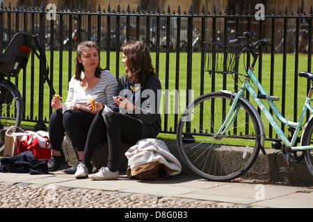 Due giovani donne sedevano a due passi tra le biciclette godendosi il sole mentre mangiavano i loro sandwich a Oxford, Oxfordshire UK nel mese di maggio Foto Stock