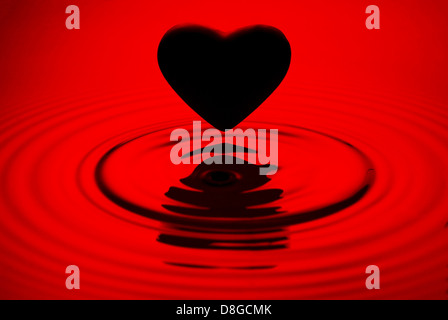 Cuore nero siluett su rosso increspature dell'acqua Foto Stock