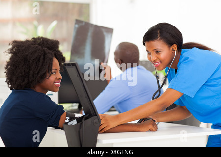 La cura dei giovani africani infermiera controllo pressione del sangue del paziente in ambulatorio medico Foto Stock