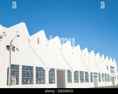 Motivo a dente di sega, il tetto del vecchio edificio industriale fornisce un bianco motivo a dente di sega contro il cielo blu. Napier della lana di vecchi capannoni. Foto Stock