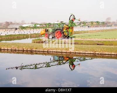 Il trattore la spruzzatura di pesticidi su campi di tulipani con la riflessione sulla superficie di un canale. Concetto di gestione del territorio e dell'ambiente. Foto Stock