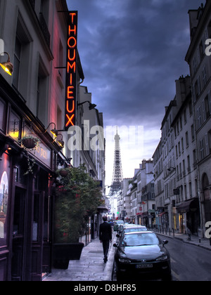 Un uomo solitario cammina lungo Rue Saint-Dominique passando davanti al ristorante Thoumieux nel 7° arrondissement di Parigi al crepuscolo, con luci rosse al neon e la Eiffel Foto Stock