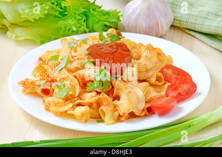 Pasta con ketchup e pomodori sulla piastra bianca sul tavolo di legno Foto Stock