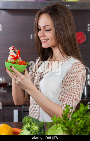 Bella e giovane donna mangia insalata in cucina domestica Foto Stock