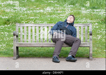 Un giovane uomo addormentato su una panchina nel parco in St Jame's Park London REGNO UNITO Foto Stock