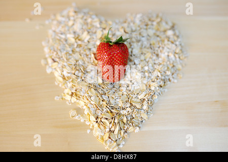 Una fragola su un mucchio di fiocchi di avena a forma di cuore Foto Stock