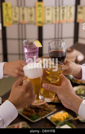 Quattro persone la tostatura gli uni con gli altri con varie bevande a Izakaya Foto Stock