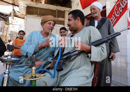 Gli uomini withe un fucile di fumare pipa ad acqua shisha in un bar in un villaggio in Alto Egitto Foto Stock