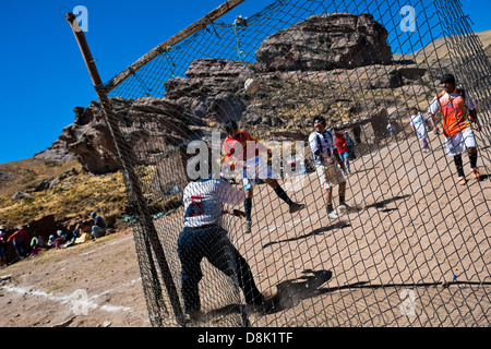 Uomini indigeni giocare a calcio su una sporcizia di calcio nelle zone rurali della Comunità di montagna vicino a Puno, Perù. Foto Stock