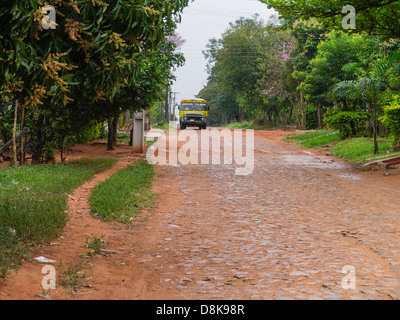 Un autobus pubblico corre lungo una strada rurale con un semi-strada asfaltata al di fuori della città di Luque, Paraguay. Foto Stock