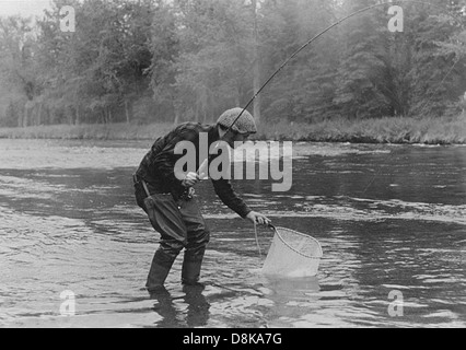Una fotografia vintage in bianco e nero che mostra un pescatore al lavoro. Il pescatore sta gettando una fila nell'acqua, probabilmente da una piccola barca. L'immagine offre uno sguardo sulle pratiche di pesca tradizionali di un'epoca passata. Foto Stock