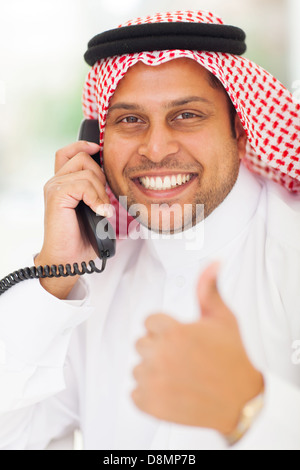 Imprenditore arabo parlando al telefono fisso e dando pollice in alto Foto Stock