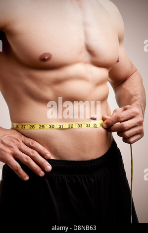 Montare l'uomo misurando la sua vita dopo un allenamento in palestra, in un colore marrone scuro dello sfondo Foto Stock