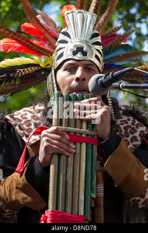 Manchester, Regno Unito. Il 1 giugno 2013. Sergio Fistely (MR) un animatore di strada in Aztec Indian Native American costume e copricapo di piume in Manchester Piccadilly godendo le varie attrazioni del centro della città con buskers peruviano, costume street muscians, giocando un accompagnamento musicale. I flauti di Pan, panpipes, syrinx, flauto sono un gruppo di strumenti musicali basati sul principio del tubo chiuso costituito da una pluralità di tubi aumentando gradualmente la lunghezza. Più varietà di panflutes sono stati a lungo popolare come strumenti folk. Il pipe in legno sono tipicamente fatti di bambù o di canna da zucchero. Foto Stock