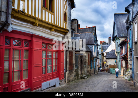 Via affascinante con le tradizionali case con travi di legno e tetti di ardesia nel villaggio bretone in Bretagna, Francia. Parete rossa in primo piano. Foto Stock